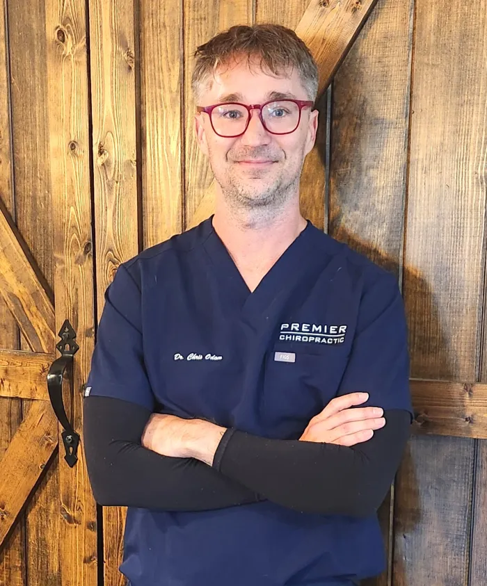 Dr. Chris Odom in red glasses and navy scrubs, arms crossed, in front of a barn wood wall
