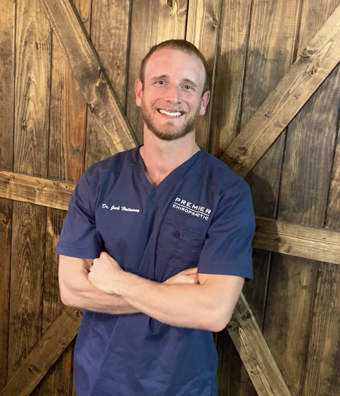 Dr. Jack Hattaway smiling in navy scrubs, arms crossed, in front of a barn wood wall